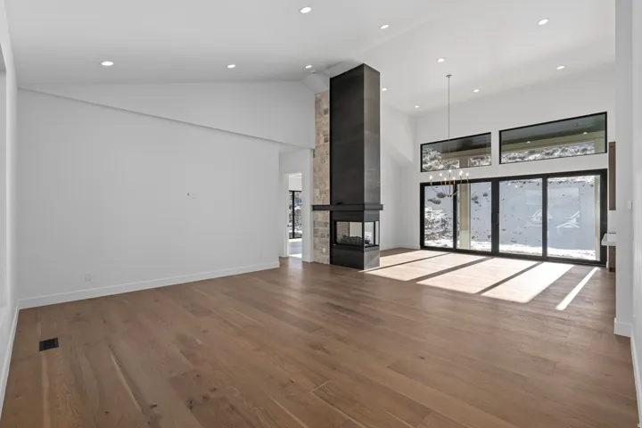 Unfurnished living room with lofted ceiling, dark wood finished floors, a multi sided fireplace, healthy amount of natural light, and hanging lights