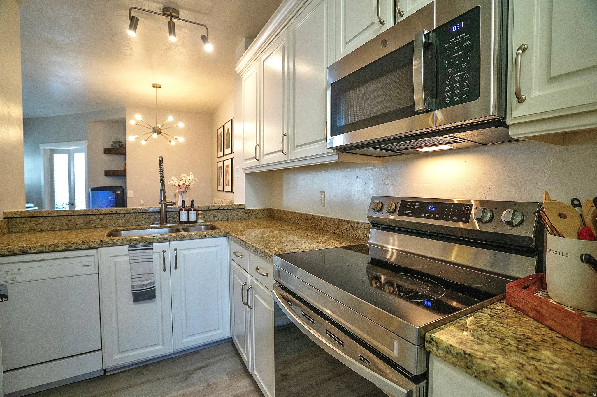 Kitchen featuring stainless steel appliances, hanging lights, white cabinetry, light stone counters, and light wood-style flooring