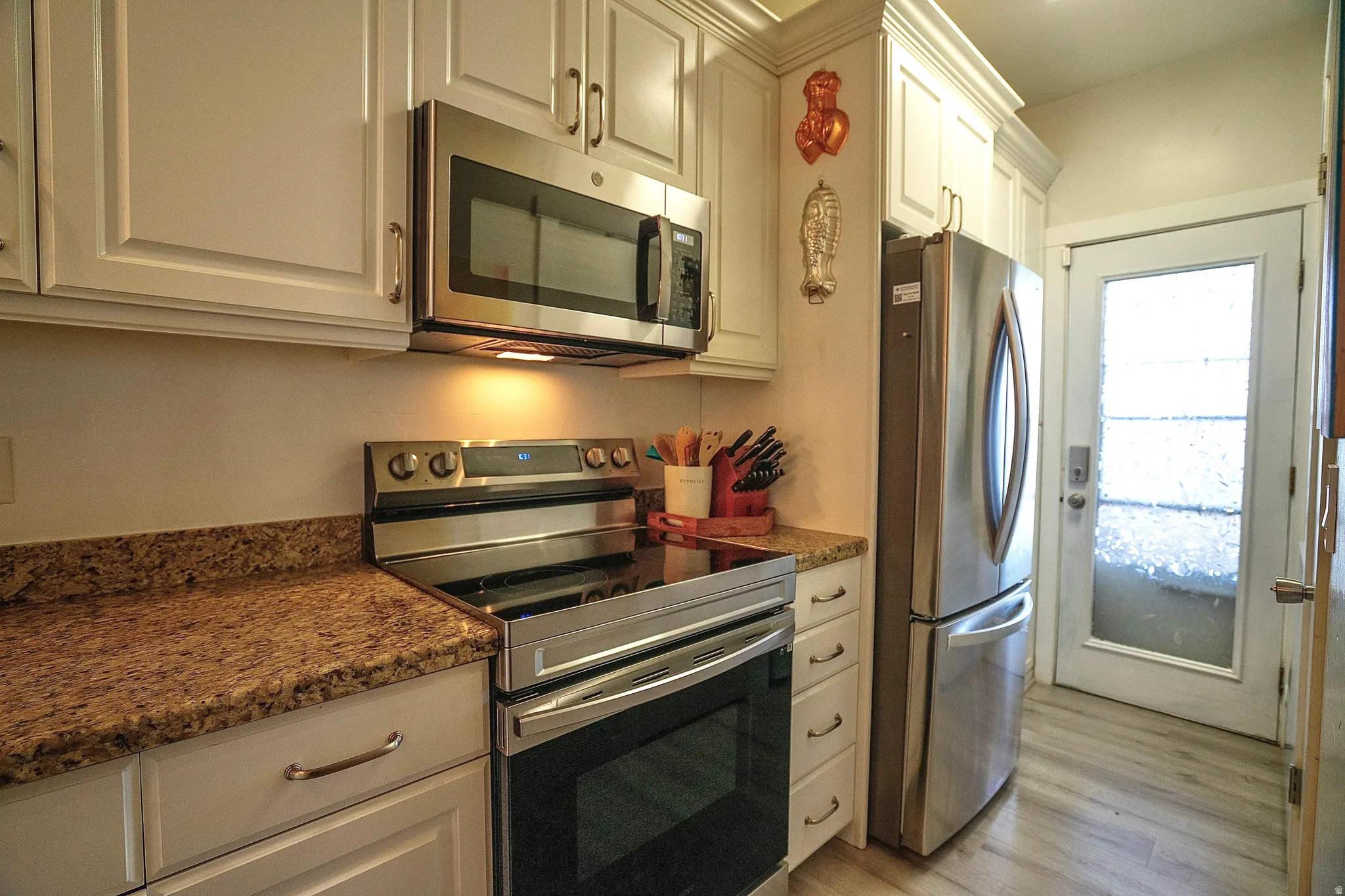 Kitchen with stainless steel appliances, white cabinetry, light wood-style floors, and dark stone countertops
