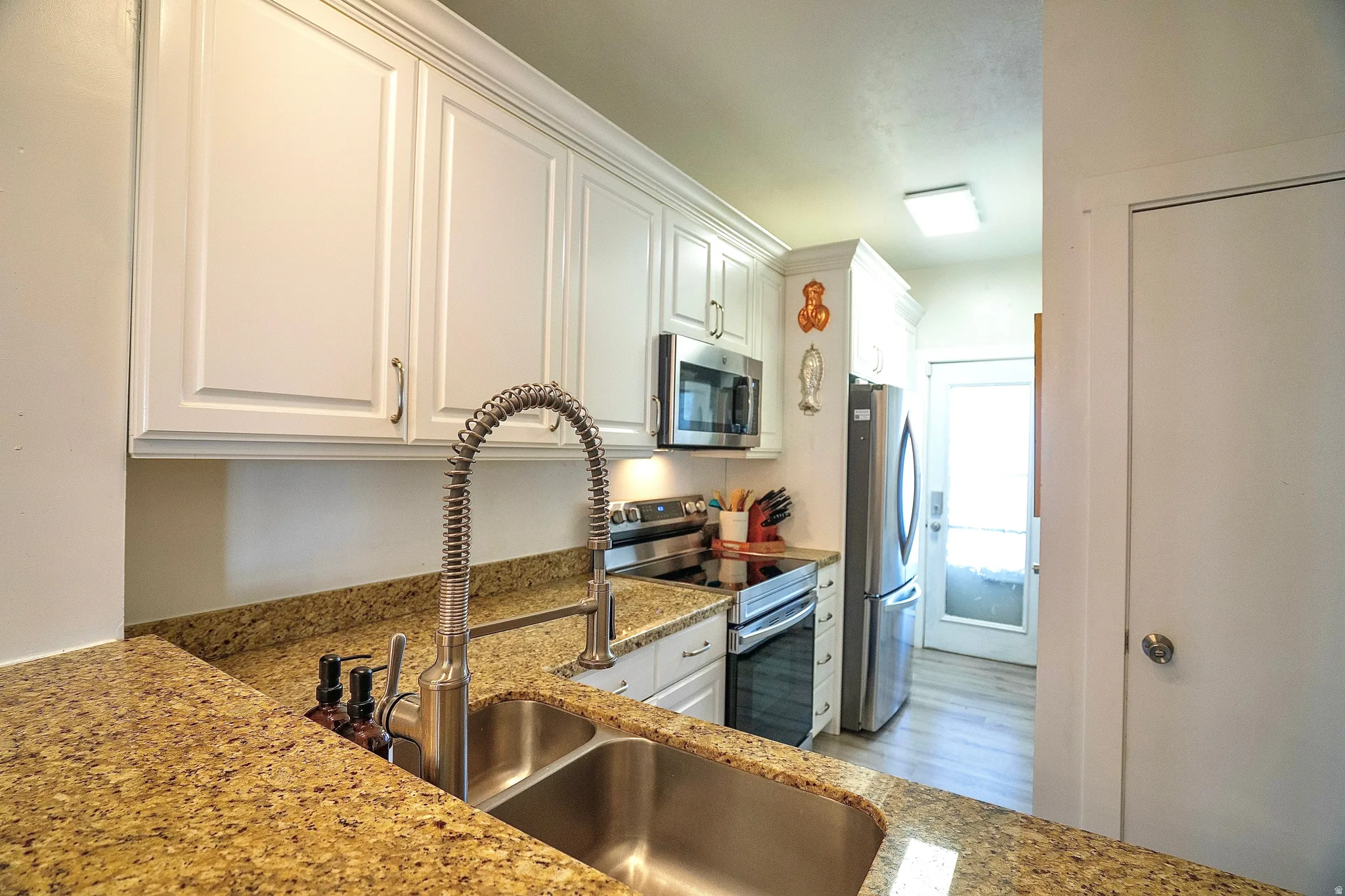 Kitchen featuring stainless steel appliances, white cabinetry, light stone countertops, and light wood finished floors