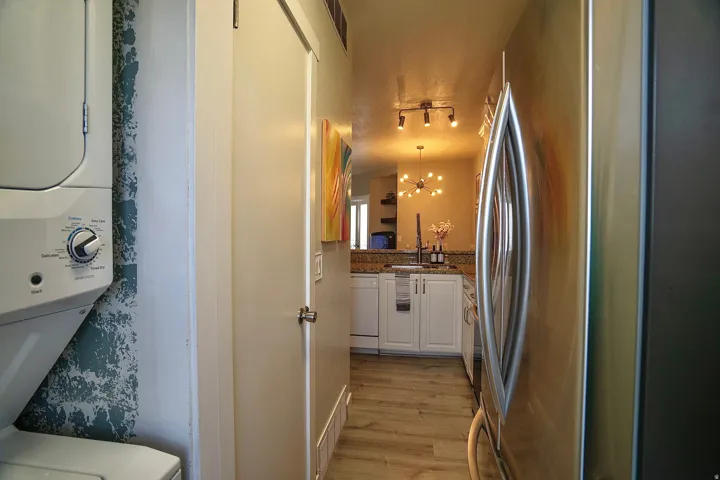 Kitchen featuring freestanding refrigerator, dark stone counters, white cabinets, stacked washing machine and dryer, and dishwasher