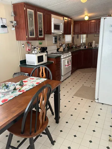 Kitchen with white appliances, dark countertops, glass fronted cabinets, and light flooring