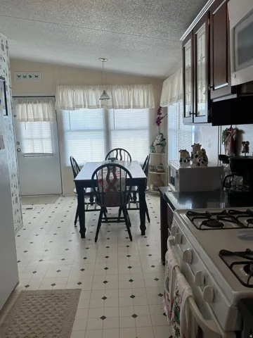 Kitchen with white appliances, light floors, pendant lighting, dark wood finish cabinetry, and dark countertops