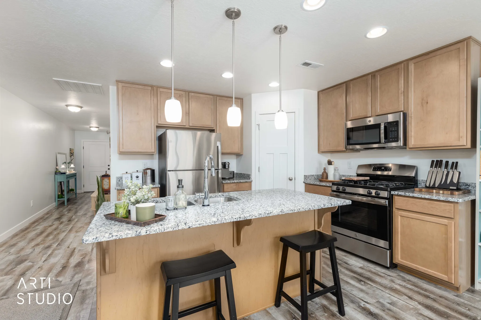 Kitchen featuring stainless steel appliances, light stone countertops, light wood-style floors, a breakfast bar area, and a kitchen island with sink