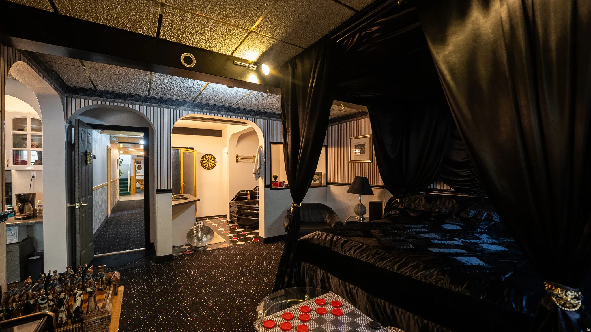 Black canopy bed with draped fabric, patterned carpet flooring, arched doorways, a built-in wet bar, and a spiral staircase
