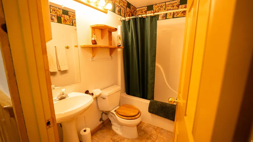 Pedestal sink, wall-mounted mirror, overhead vanity lighting, shower/tub combination, and wall shelving