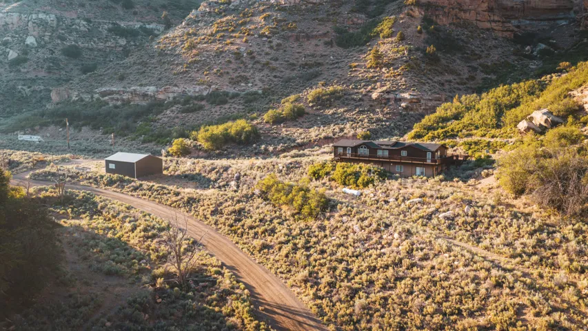 Expansive mountain property featuring a multi-level residence with a large exterior deck, a detached structure, and a winding dirt road