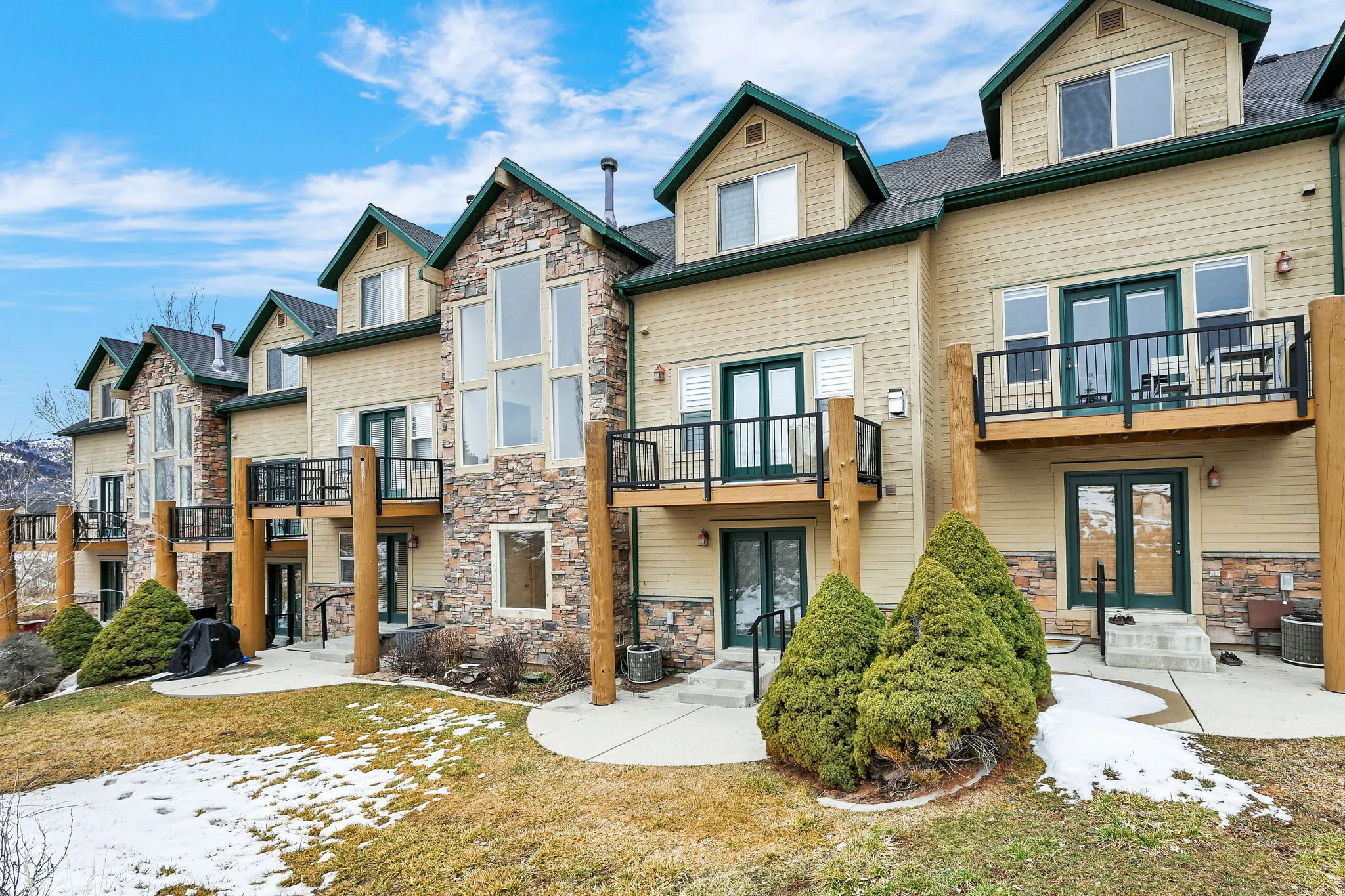 Snow covered rear of property featuring french doors, a patio area, stone siding, and a balcony
