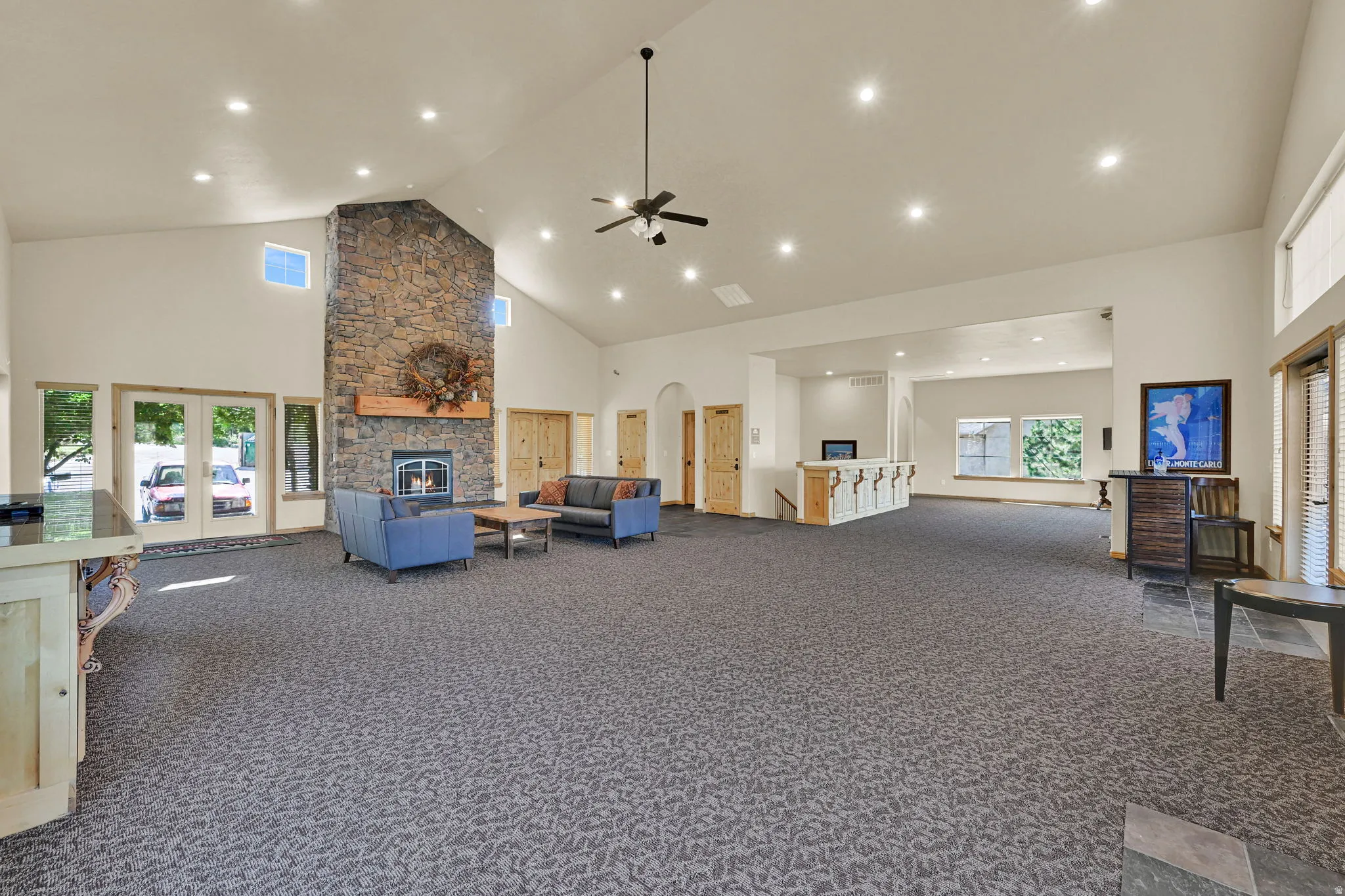 Living room featuring a high ceiling, ceiling fan, dark colored carpet, recessed lighting, and a stone fireplace