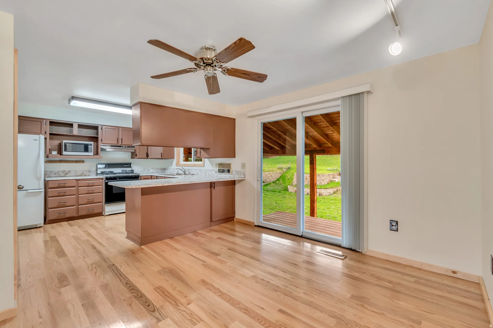 Kitchen with gas stove, freestanding refrigerator, ceiling fan, a peninsula, and light wood-style floors