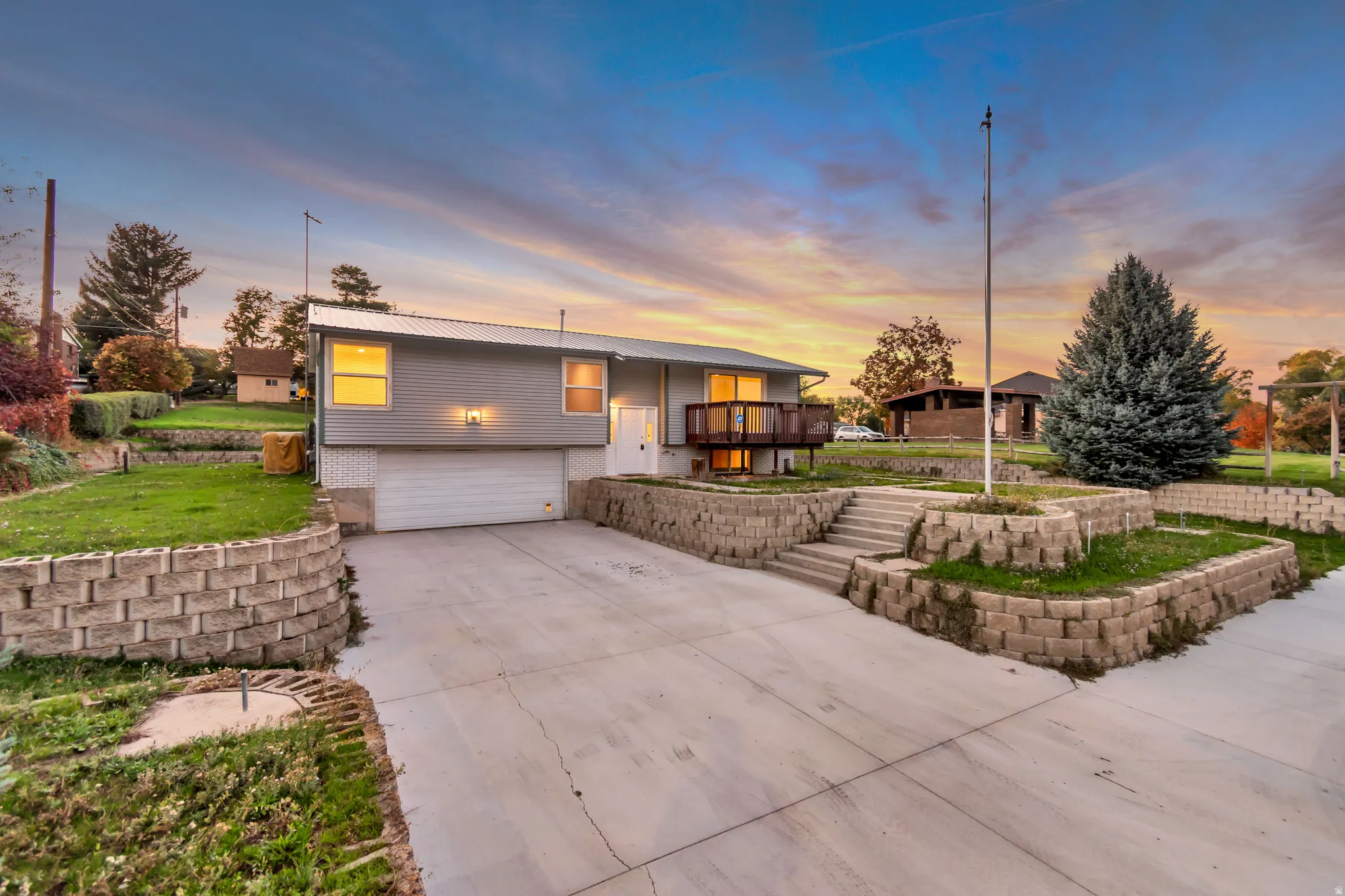 Split foyer home featuring an attached garage, concrete driveway, brick siding, a patio, and a metal roof