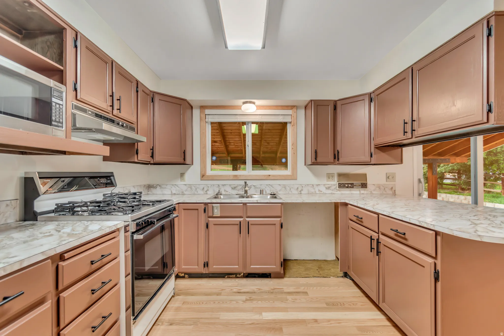 Kitchen with gas range oven, light countertops, light wood-type flooring, stainless steel microwave, and open shelves
