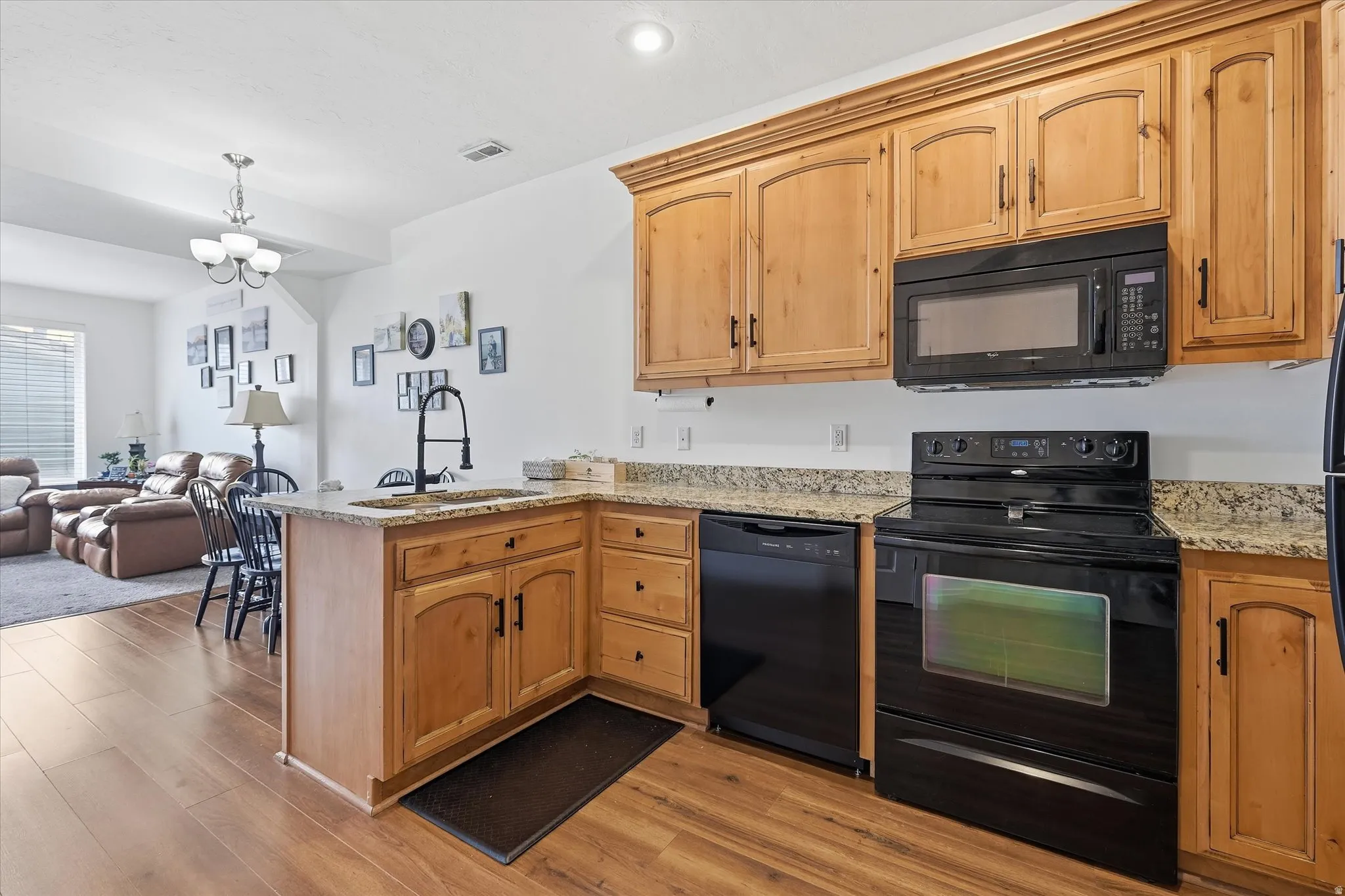 Kitchen with a peninsula, black appliances, suspended lighting, light stone countertops, and open floor plan