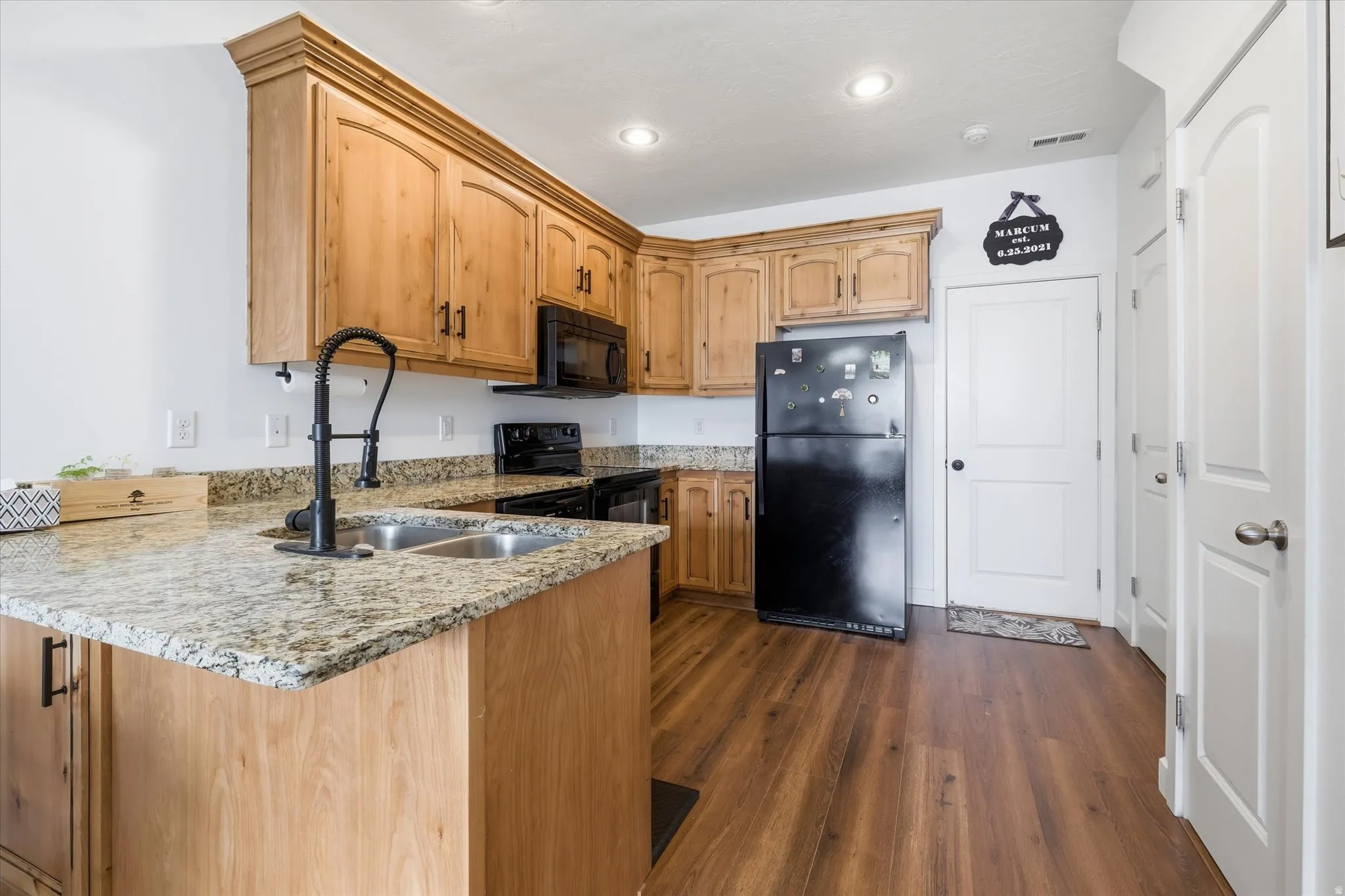 Kitchen featuring light stone countertops, black appliances, a peninsula, dark wood-style flooring, and recessed lighting