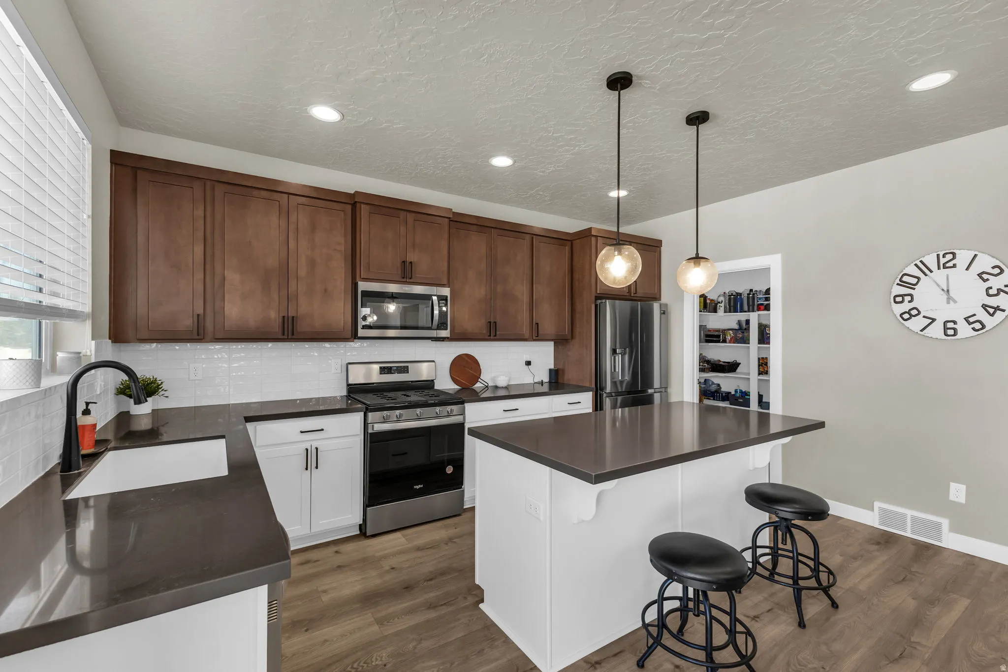 Kitchen featuring stainless steel appliances, a kitchen breakfast bar, hanging light fixtures, dark wood finished floors, and a textured ceiling