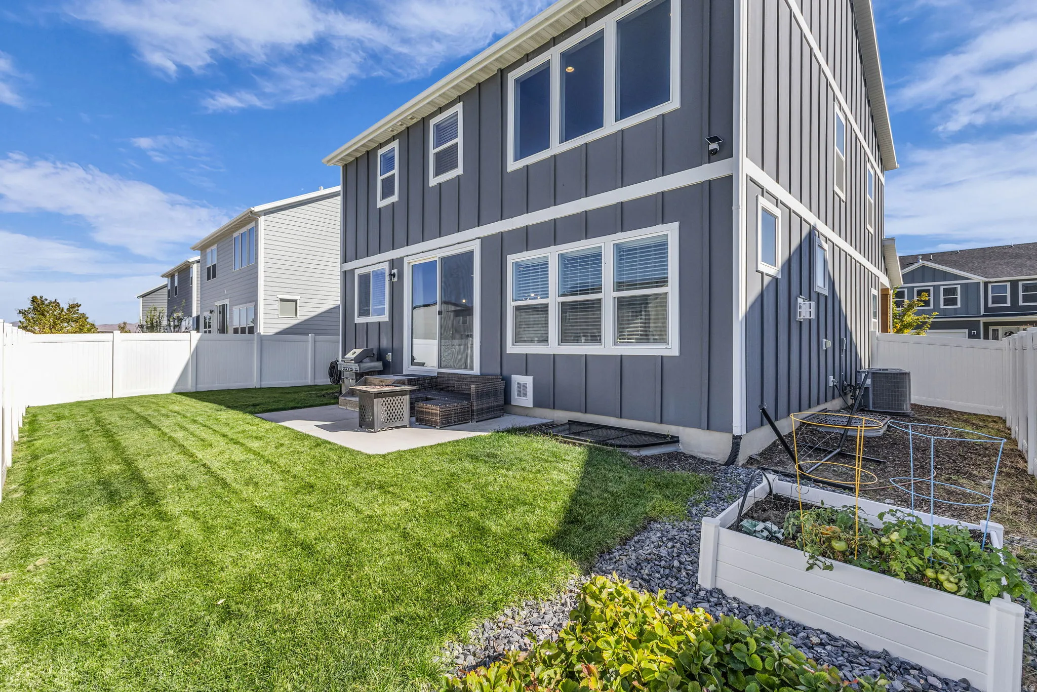 Rear view of property featuring board and batten siding, a vegetable garden, a fenced backyard, and a patio