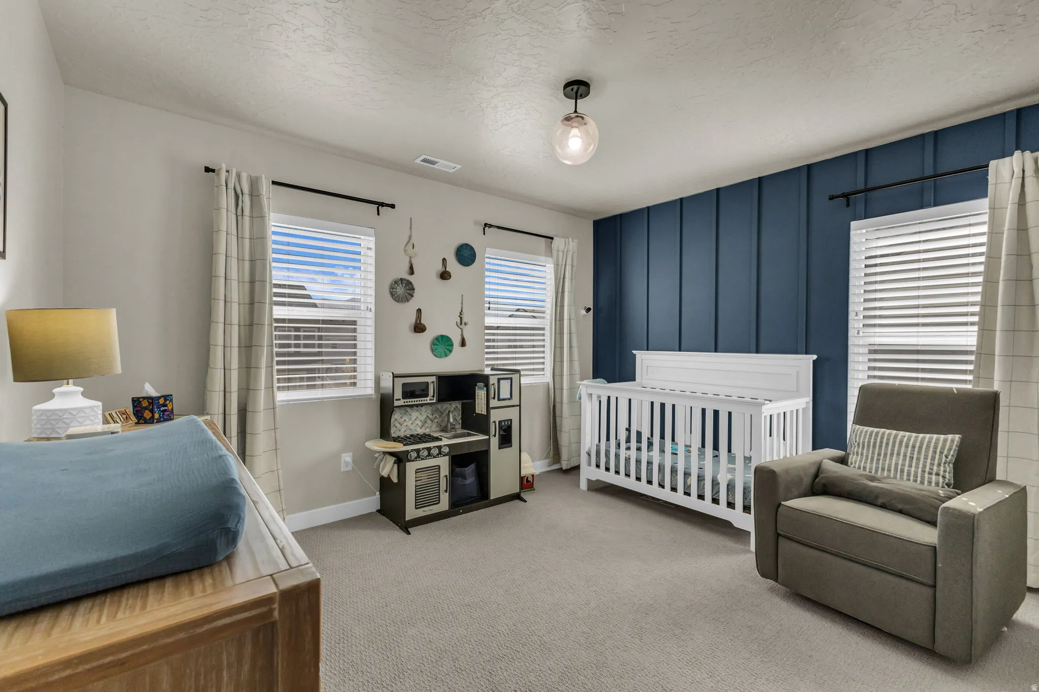 Bedroom with light colored carpet, a textured ceiling, and a nursery area
