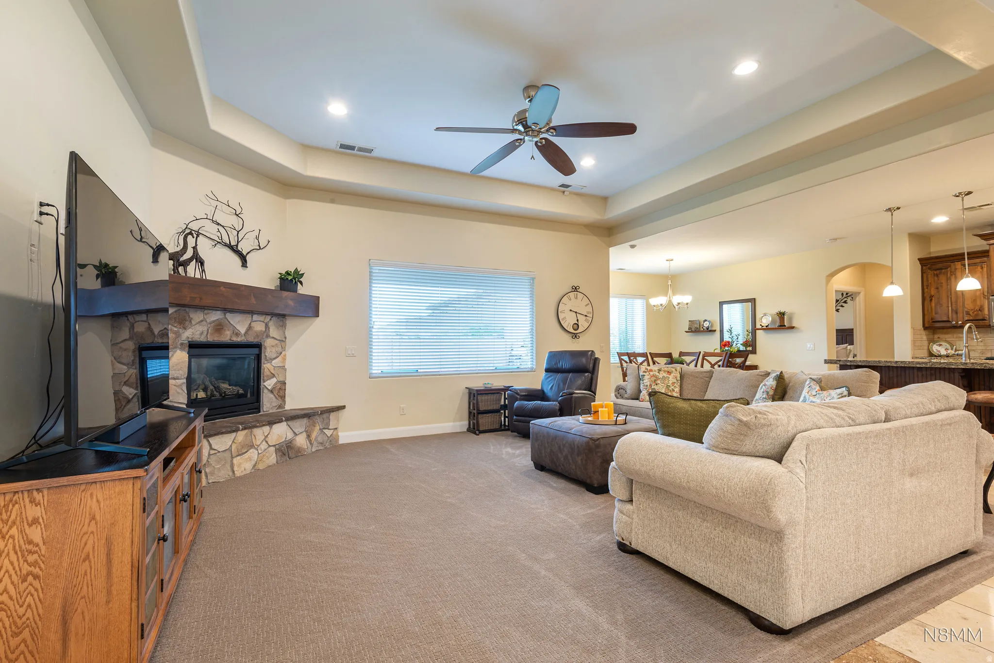Living room featuring a ceiling fan, arched walkways, a raised ceiling, light colored carpet, and a stone fireplace