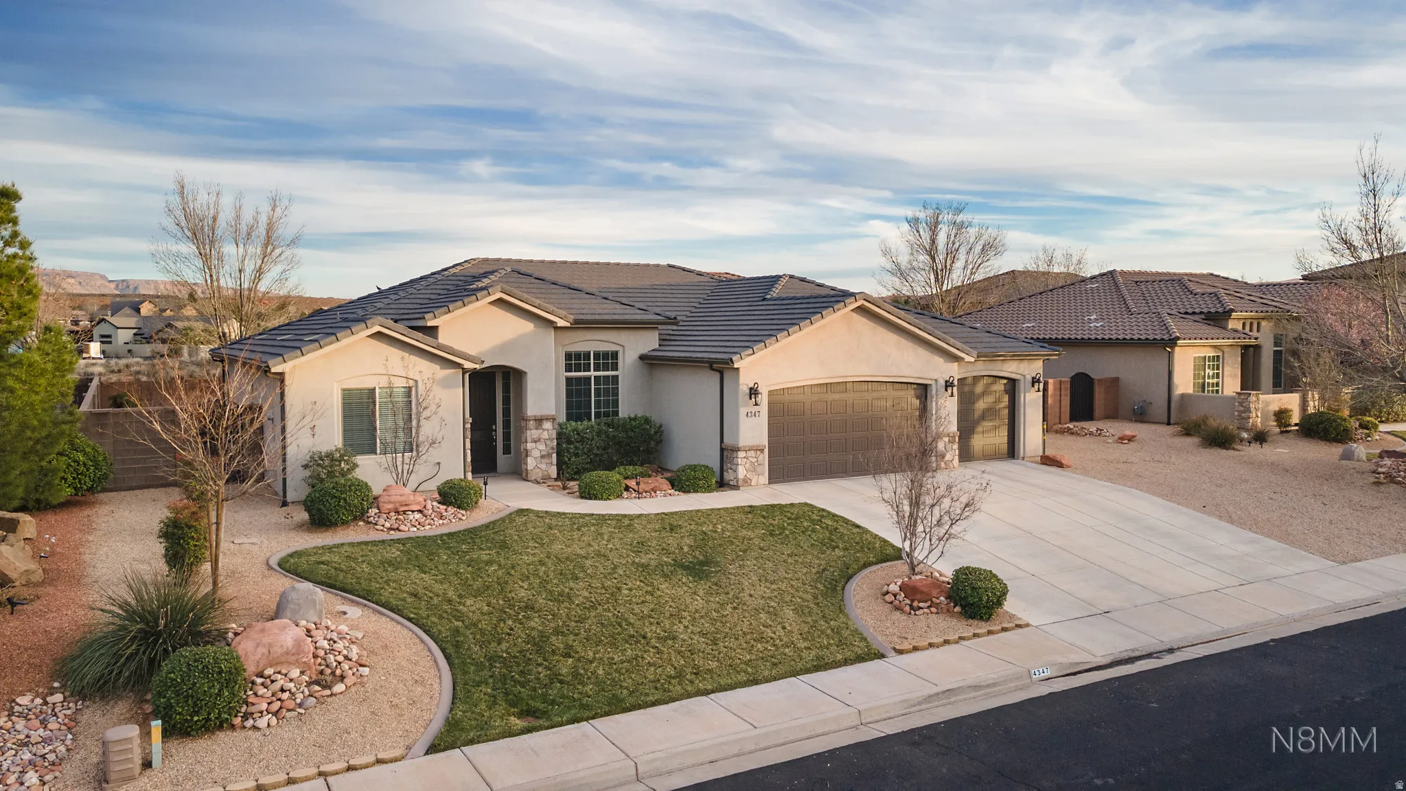 View of front of property featuring a garage, stucco siding, driveway, a tile roof, and stone siding