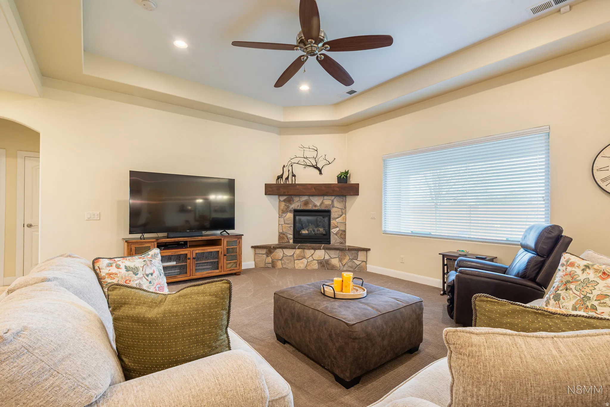 Carpeted living area with ceiling fan, arched walkways, a raised ceiling, a fireplace, and recessed lighting
