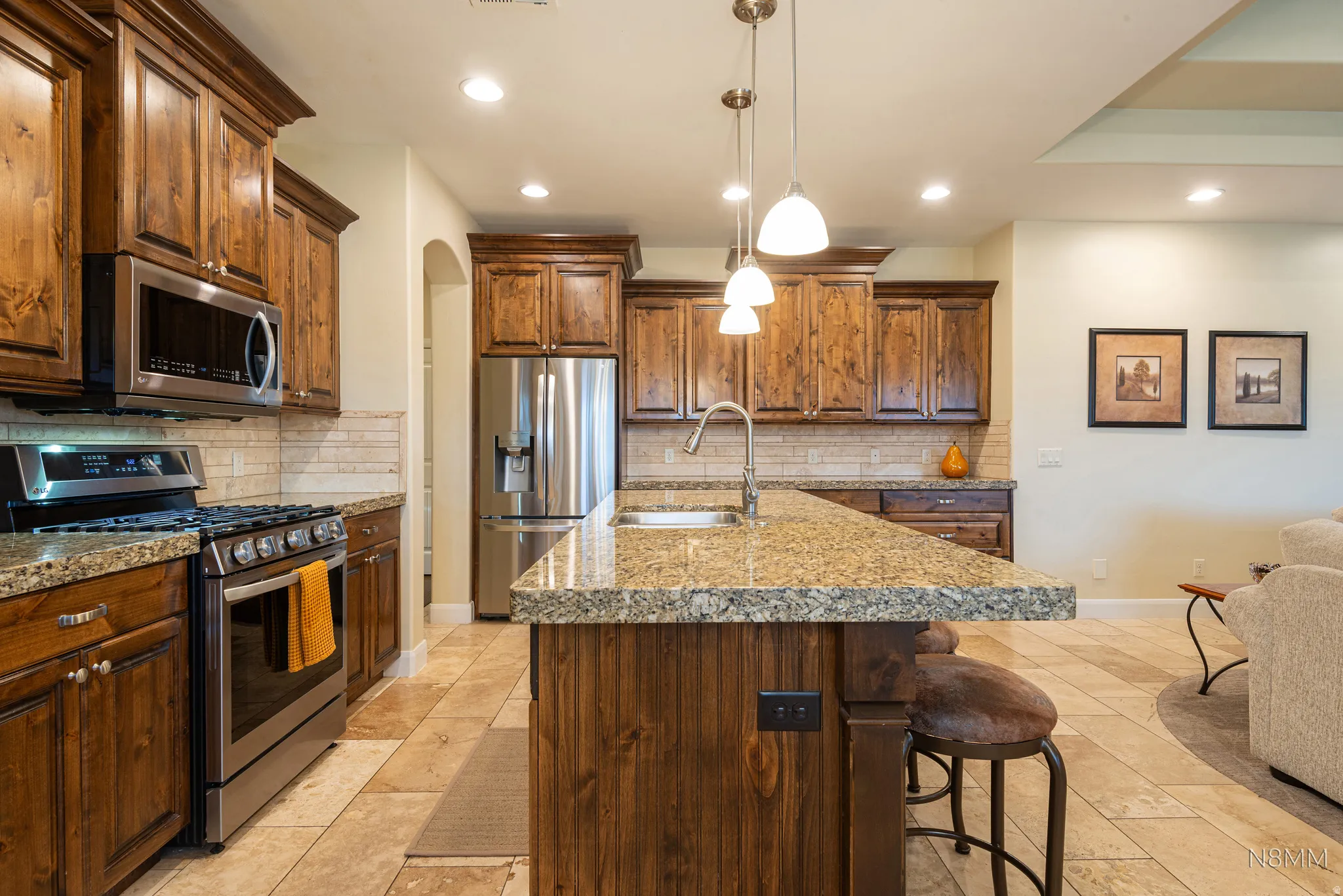 Kitchen featuring stainless steel appliances, pendant lighting, a kitchen breakfast bar, a kitchen island with sink, and tasteful backsplash