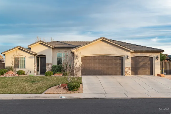 View of front of house featuring stone siding, a garage, concrete driveway, and stucco siding