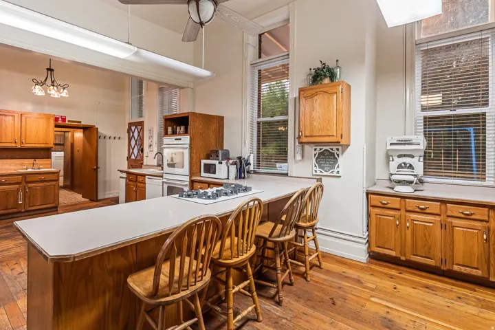 Kitchen with wood finish cabinets, light countertops, light wood-type flooring, white appliances, and a peninsula