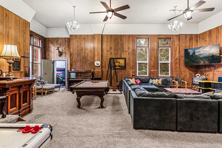 Carpeted living area with ceiling fan, suspended lighting, a textured ceiling, wooden walls, and billiards table