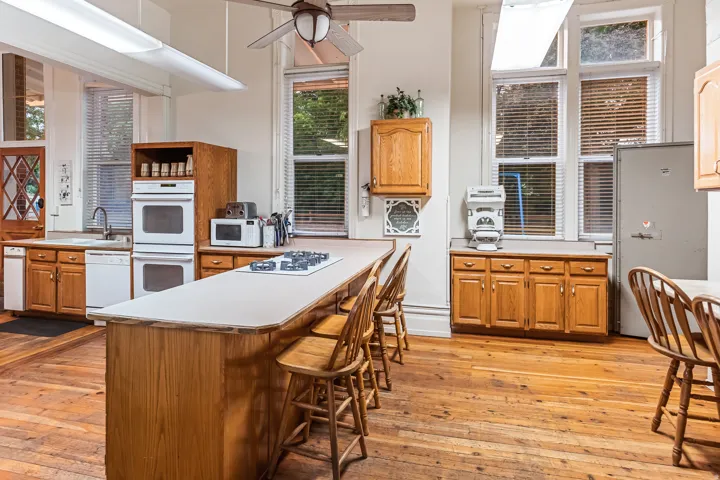 Kitchen with white appliances, light wood finished floors, light countertops, a kitchen breakfast bar, and a ceiling fan
