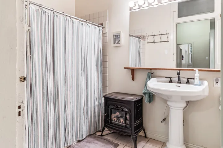 Full bathroom featuring a wood stove, a shower with curtain, and light tile patterned floors