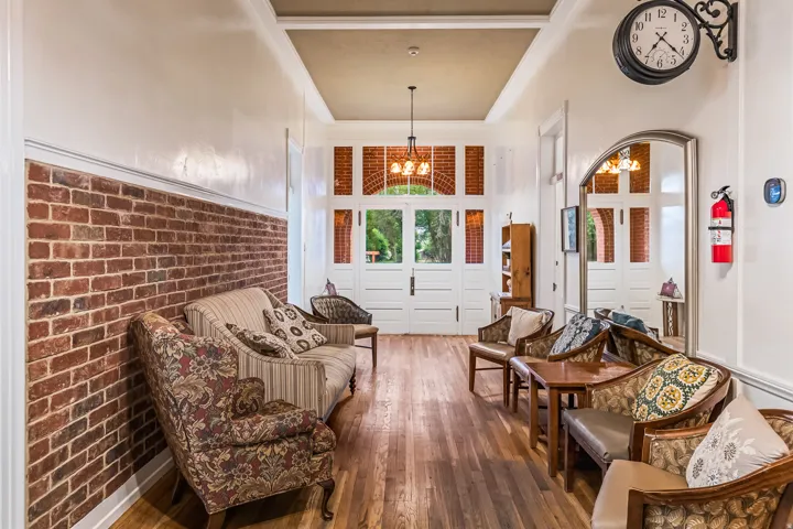 Living area with brick wall, dark wood-type flooring, a high ceiling, and suspended lighting