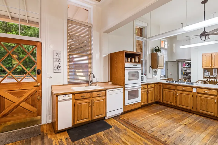 Kitchen with light wood-style flooring, white appliances, light countertops, wood finish cabinets, and a high ceiling