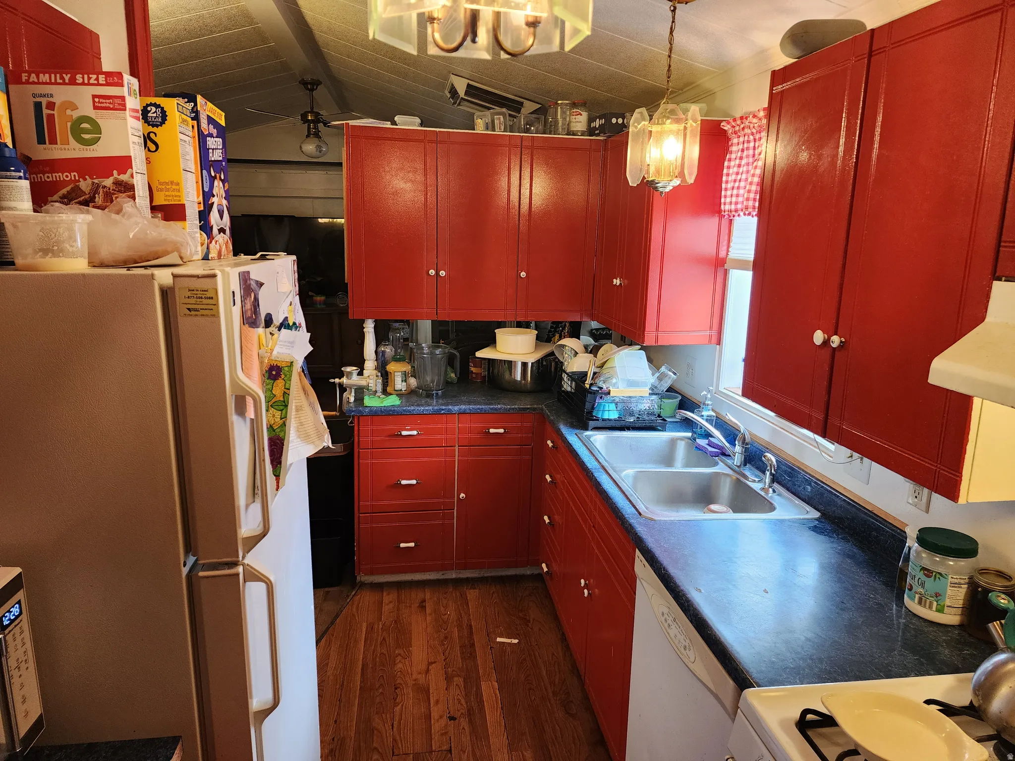 Kitchen with white appliances, dark countertops, dark wood-style floors, lofted ceiling, and range hood