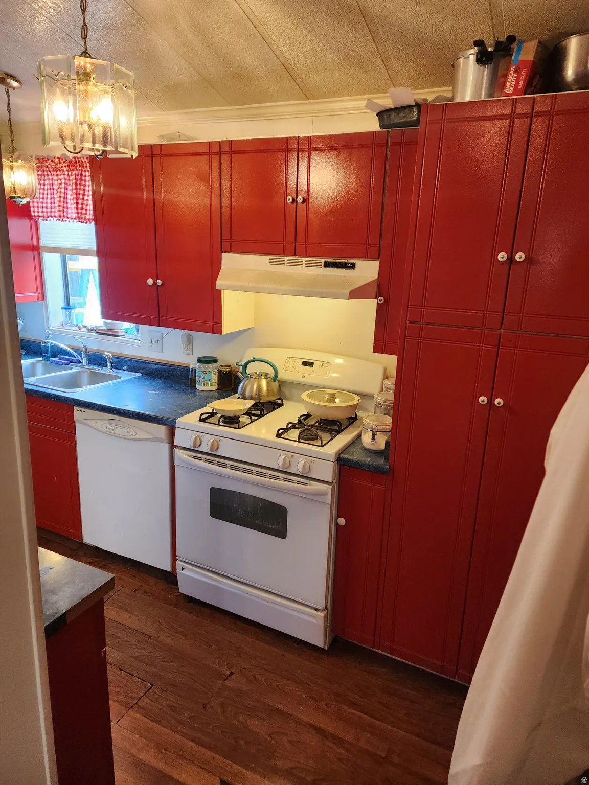 Kitchen with white appliances, dark wood finished floors, a textured ceiling, dark countertops, and red cabinets