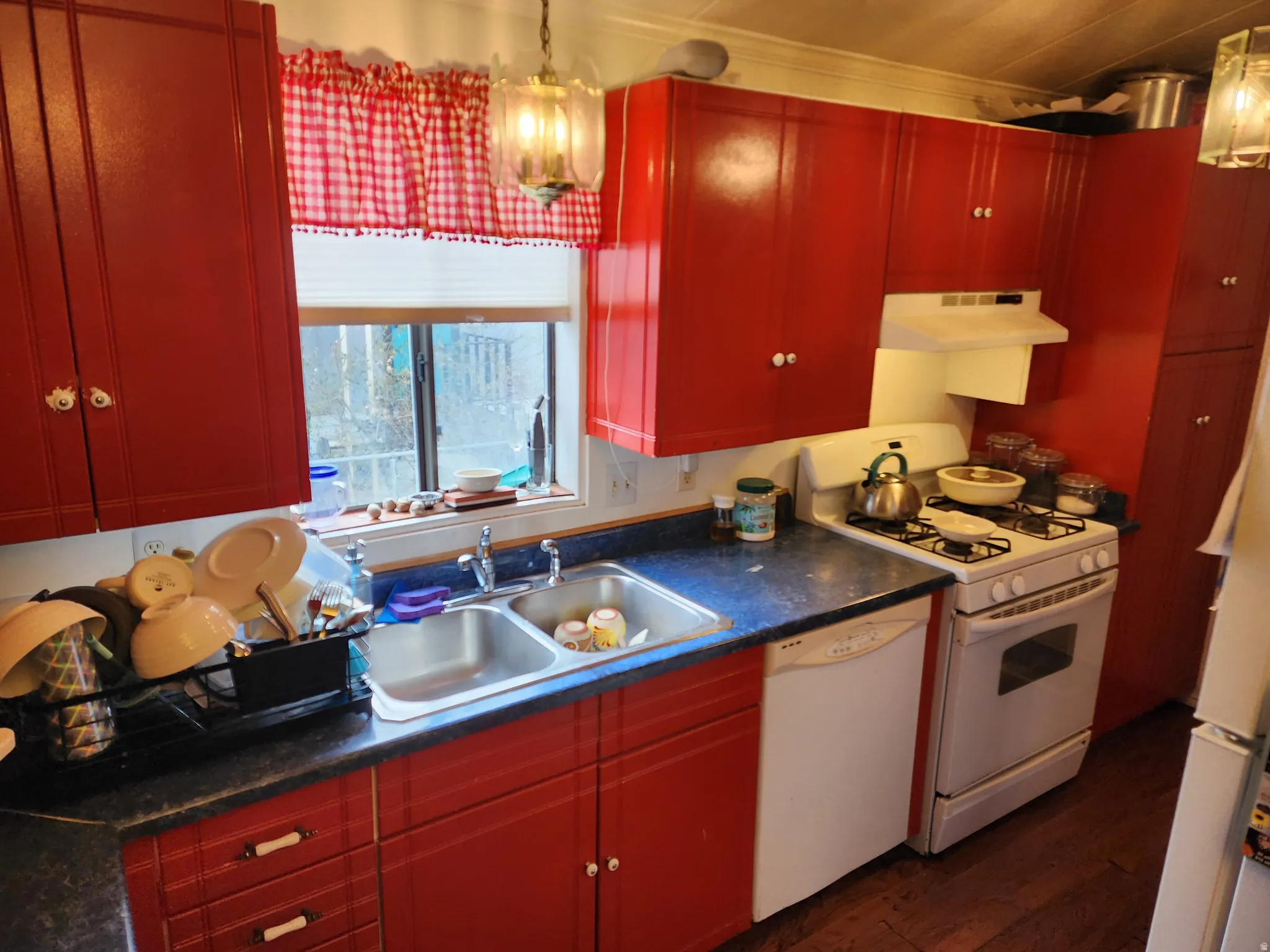 Kitchen featuring white appliances, dark wood finished floors, ventilation hood, dark countertops, and red cabinets