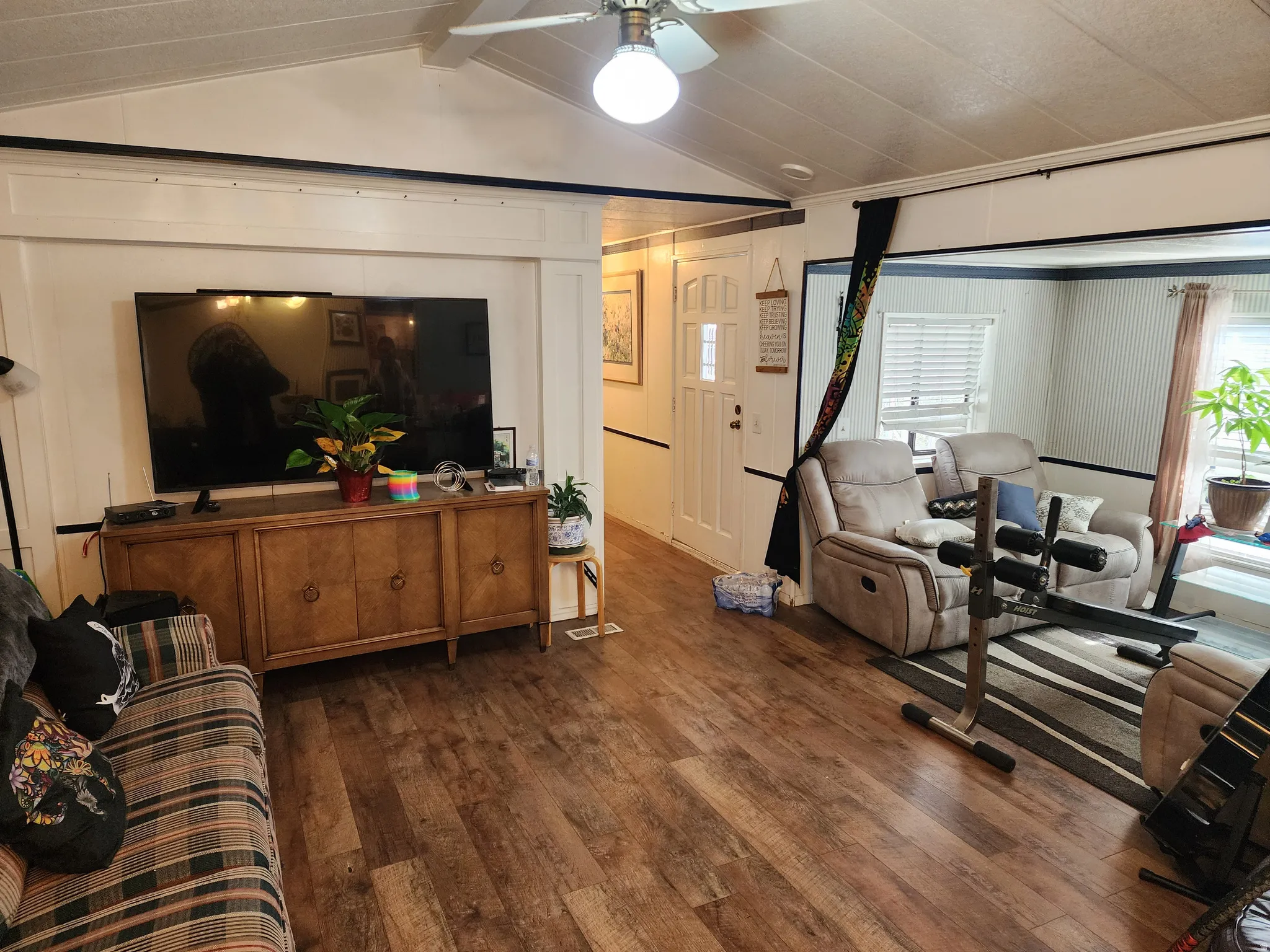 Living room featuring dark wood-style floors, a ceiling fan, beamed ceiling, and a decorative wall
