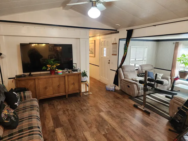 Living room featuring dark wood-style floors, a ceiling fan, beamed ceiling, and a decorative wall