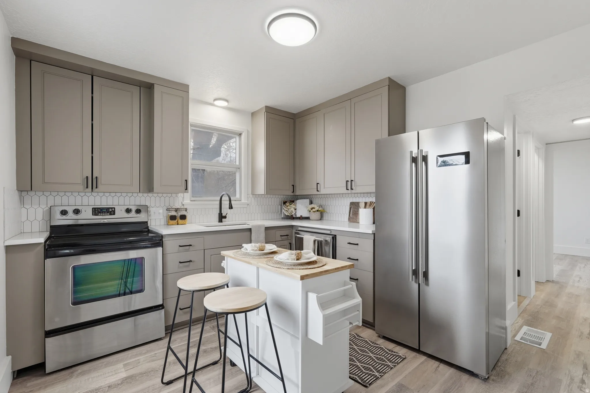 Kitchen featuring gray cabinets, stainless steel appliances, light wood finished floors, and backsplash