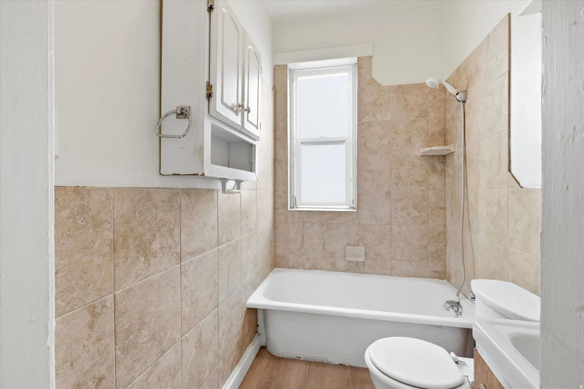 Bathroom with tile walls, bathtub / shower combination, vanity, and light wood-style floors