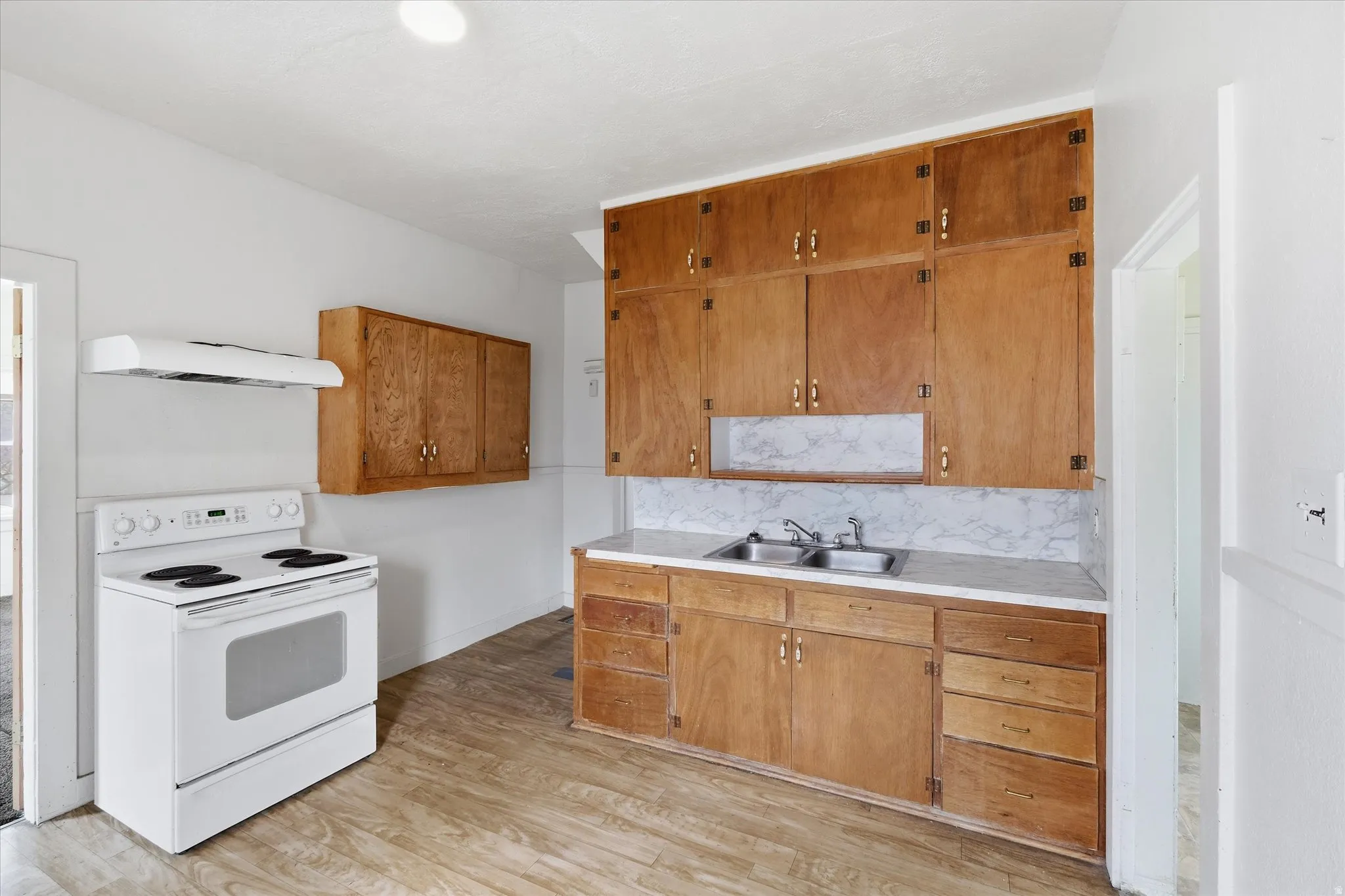 Kitchen featuring electric stove, light countertops, wood finish cabinets, light wood-type flooring, and ventilation hood