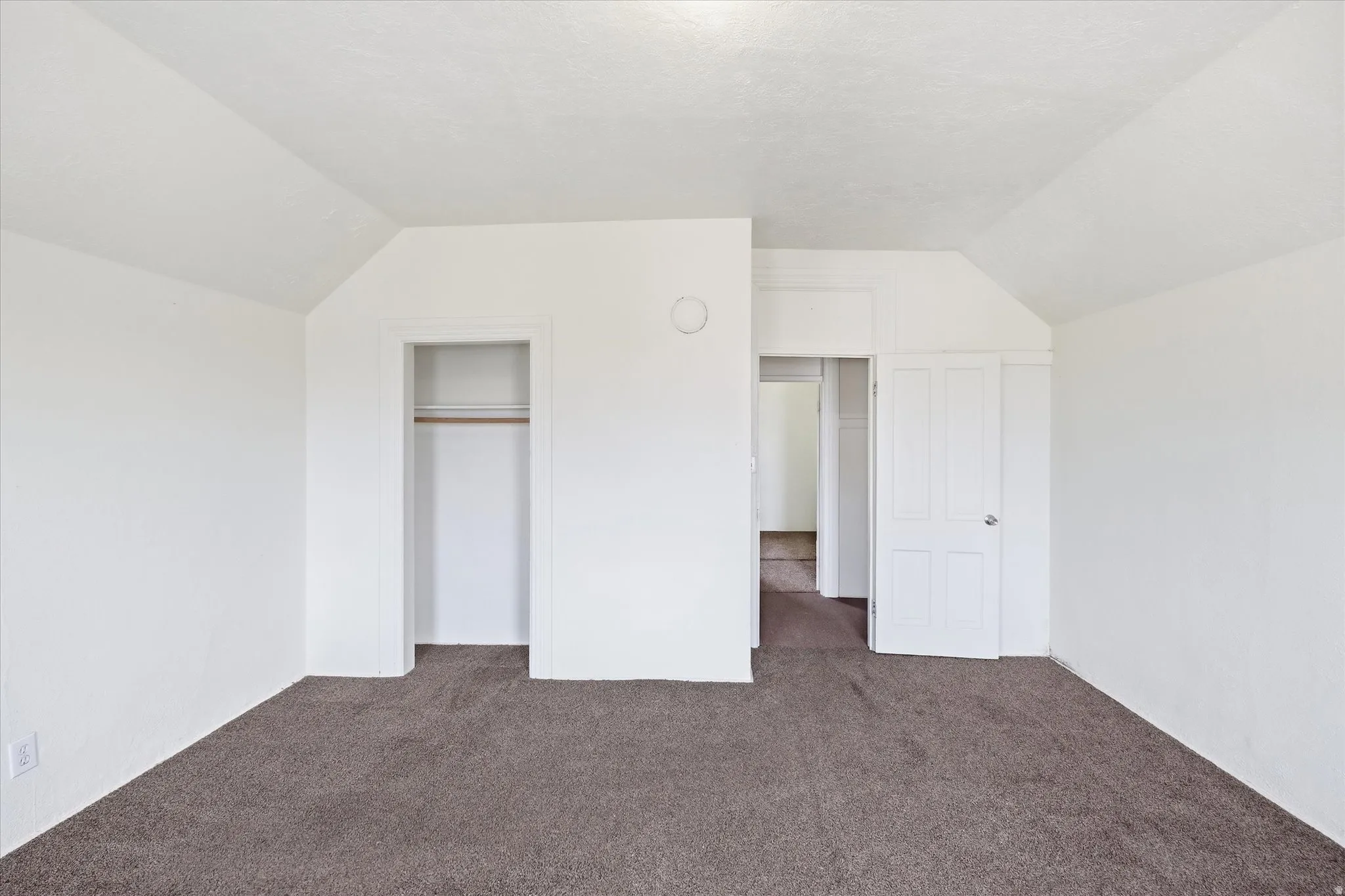 Unfurnished bedroom featuring vaulted ceiling, dark colored carpet, and a closet
