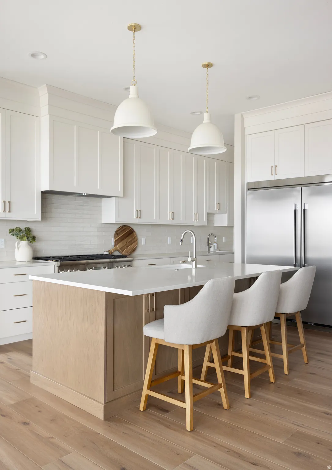 Kitchen with built in refrigerator, two tone color scheme, a large island with sink, decorative light fixtures, and light wood finished floors