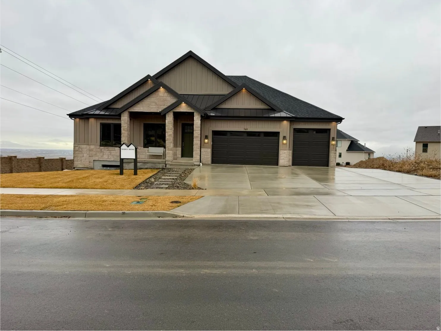 View of front of home featuring a standing seam roof, stone siding, an attached garage, covered porch, and concrete driveway