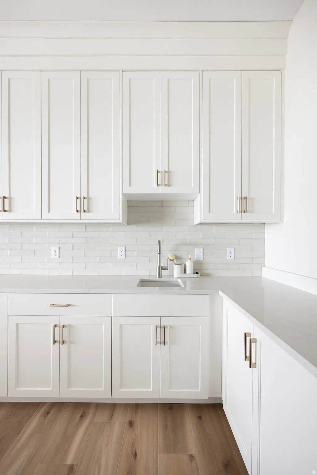 Kitchen featuring white cabinets, light stone counters, light wood-type flooring, and tasteful backsplash
