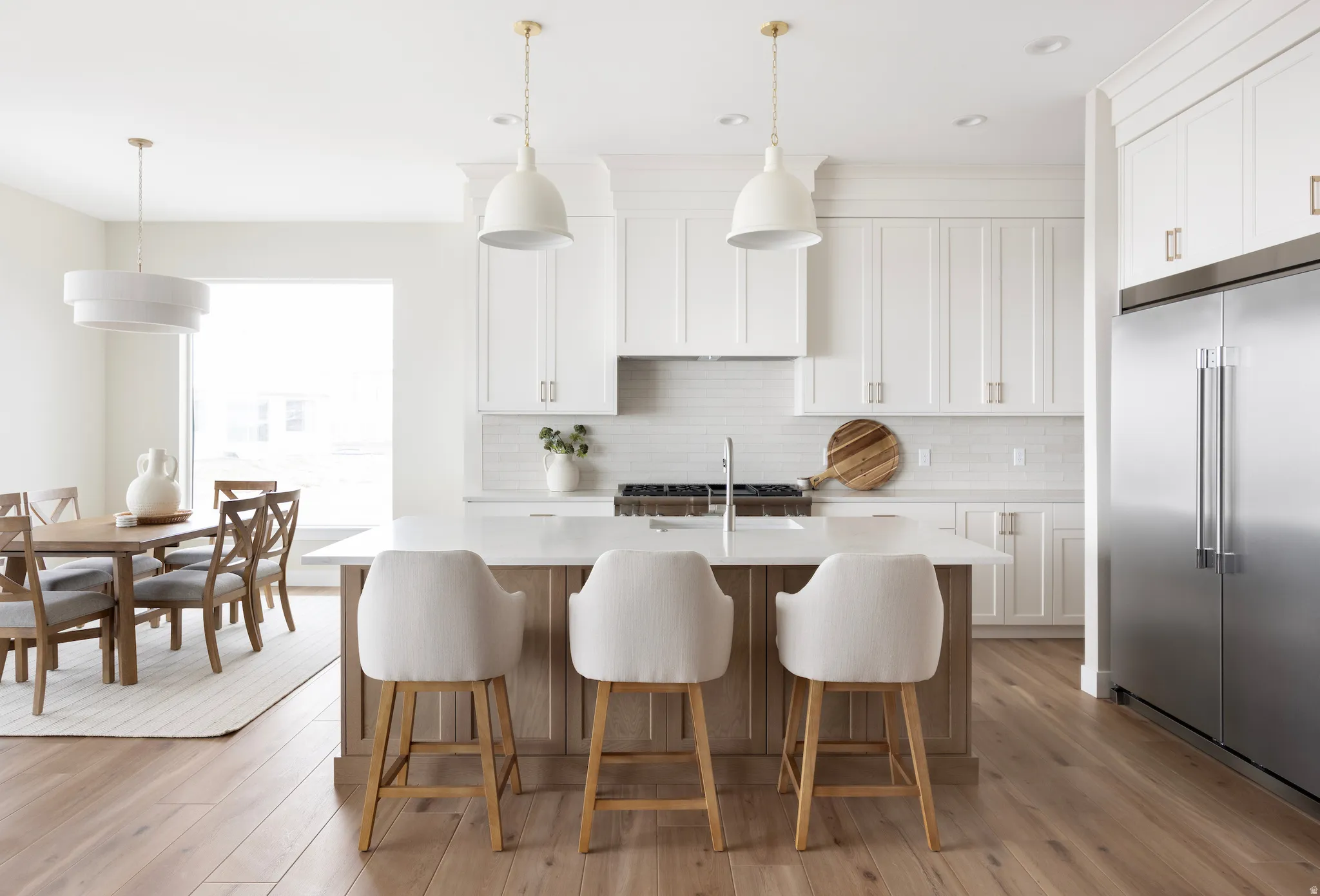 Dual tone kitchen featuring high quality fridge, light wood-style flooring, a center island with sink, a kitchen bar, and dual tone cabinetry