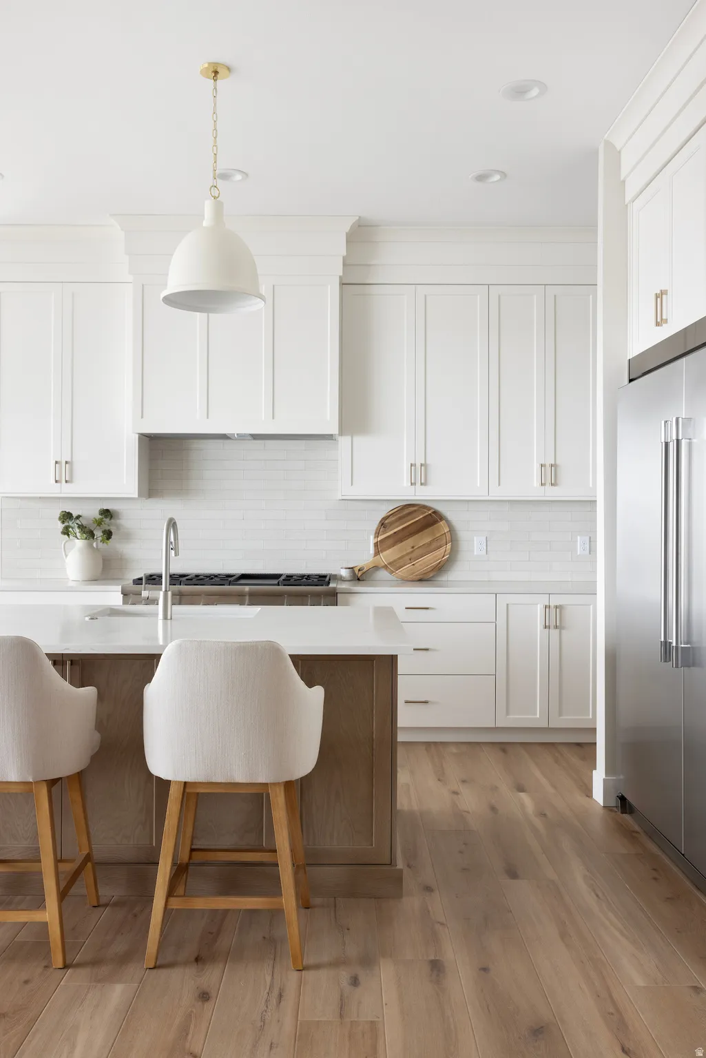 Kitchen featuring light wood-style floors, high end refrigerator, a breakfast bar area, two tone cabinets, and hanging light fixtures
