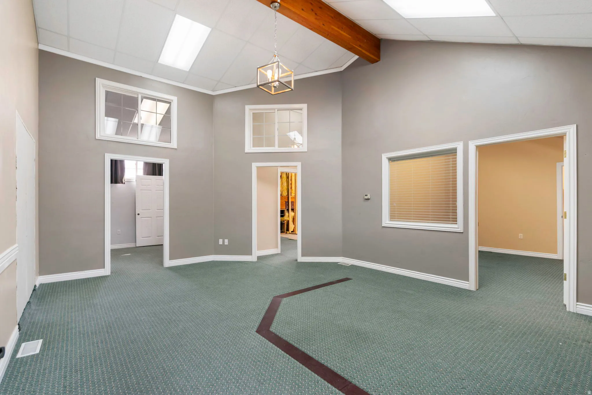 Unfurnished room with dark carpet, lofted ceiling, suspended lighting, and a drop ceiling