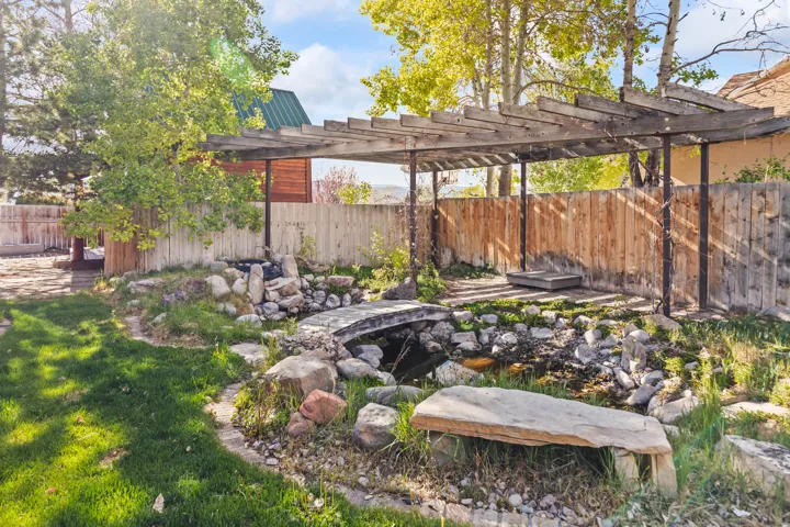 Backyard featuring a wooden pergola structure, a rock-lined water feature with a stone bridge, and a natural stone bench