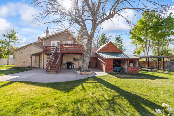 Spacious backyard featuring a brick paver patio, an elevated wood deck with stairs, and a detached shed structure