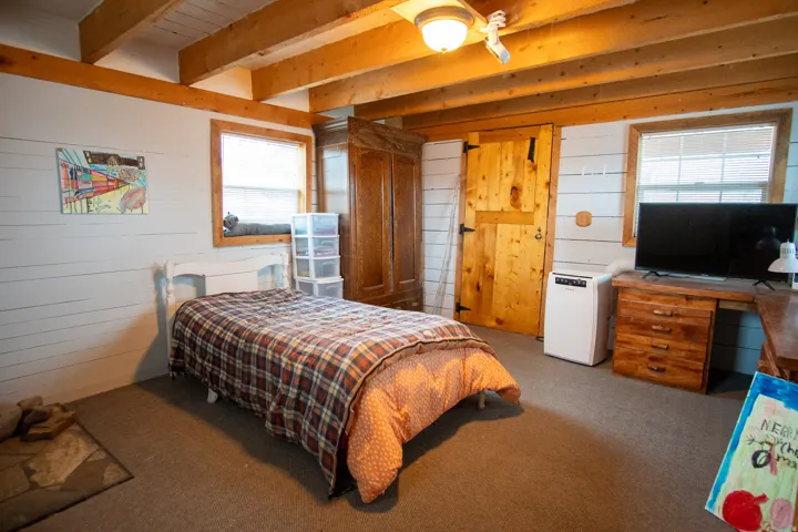 ADU main floor bedroom with wood walls, carpet flooring, beamed ceiling, and an office area as well as its own gas stove